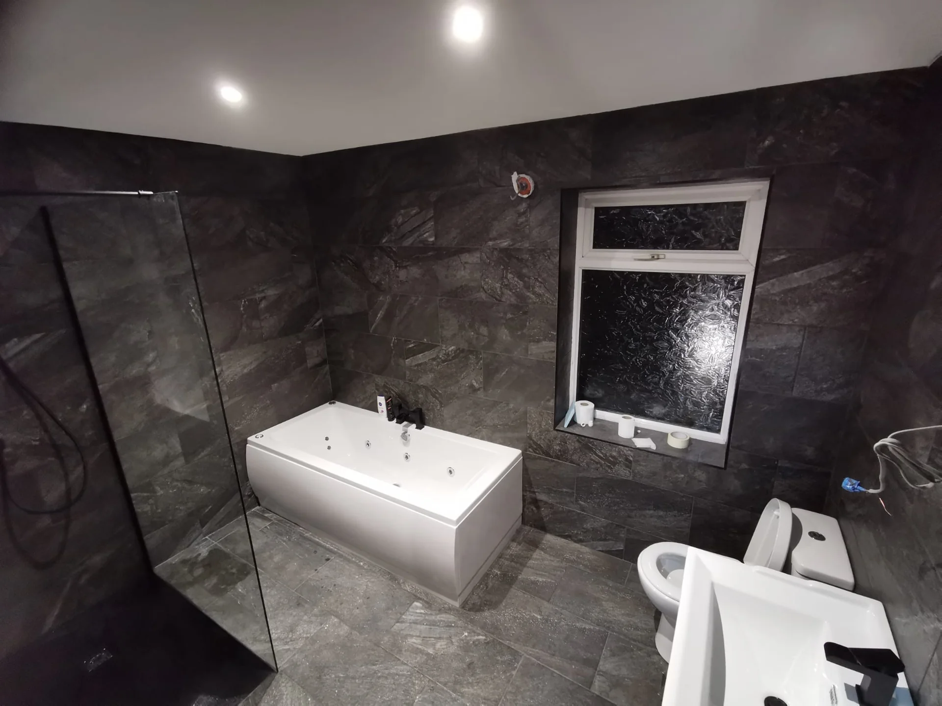 Large-format dark bathroom tiles around a bath and vanity